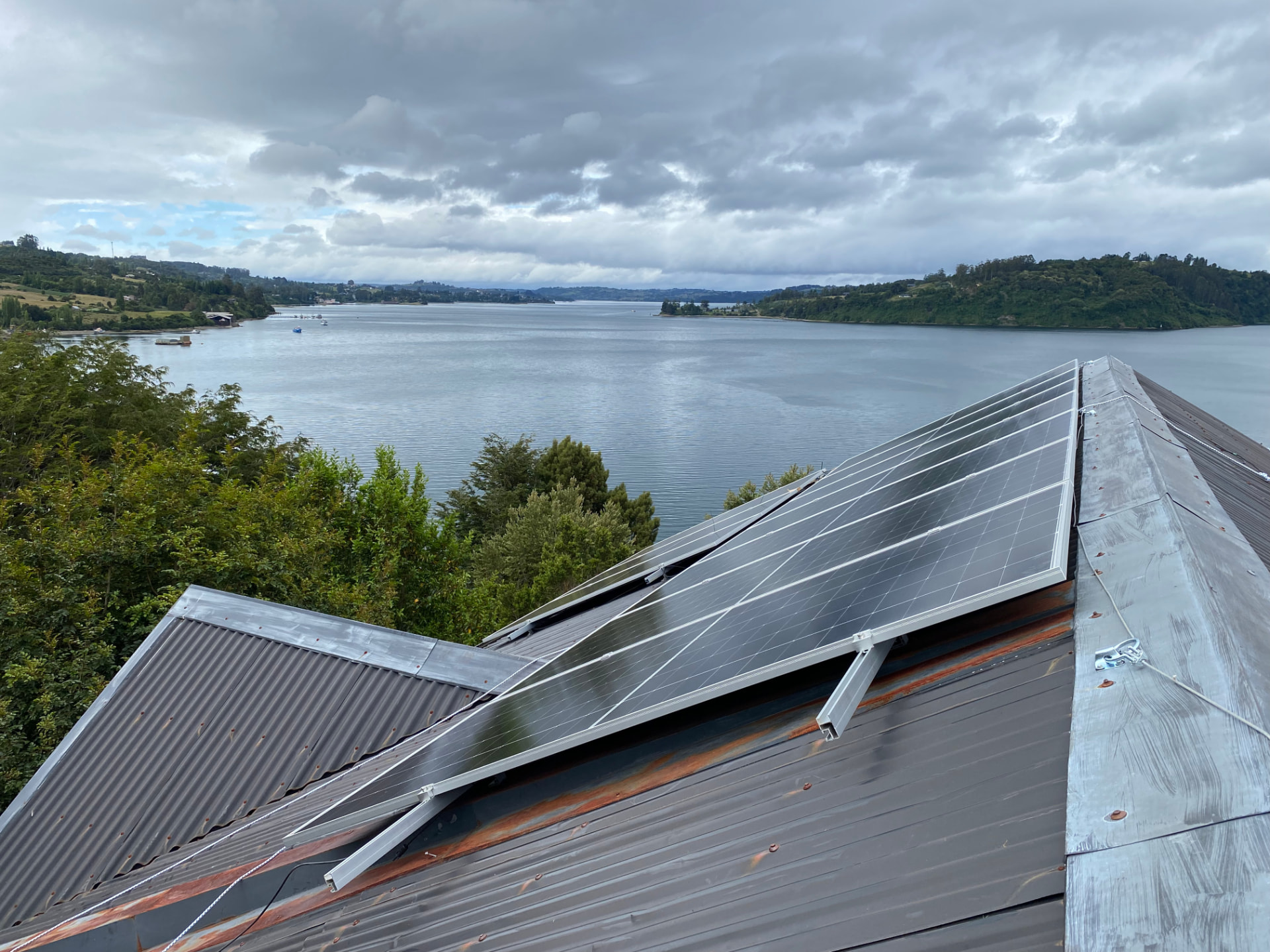 Paneles solares sobre techo de zinc frente a un canal en Chiloé